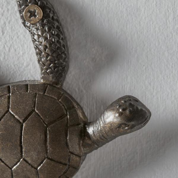 Close-up detail of an antique bronze cast iron turtle hook showing the textured skin on the head and flipper with a visible mounting screw.