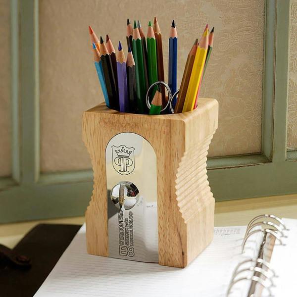 A giant wooden pencil sharpener desk tidy filled with colourful colouring pencils on a home office desk.