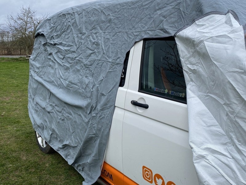 The VW T25/T3/T4/T5/T6 Campervan Cover Grey by OLPRO on a VW T5 Campervan in a field with the zip zipped up to access the campervan door.