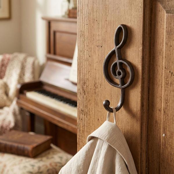 Small antique cast iron treble clef coat hook on a painted wall, highlighting its intricate musical design and vintage finish in a cozy entryway.