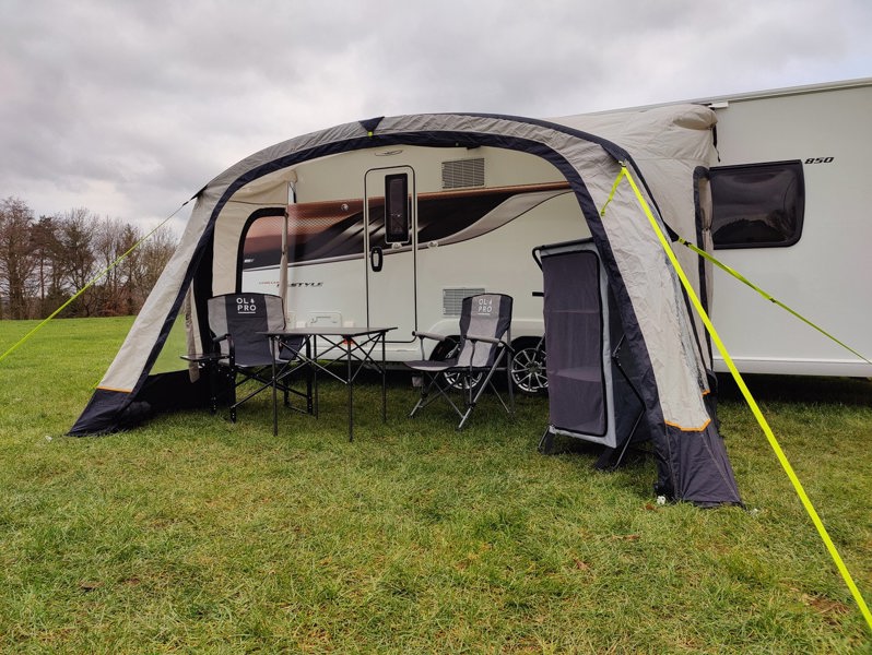 The OLPRO View Lite Breeze 390 Caravan Awning pictured in a Caravan site attached to a caravan with  some camping furniture on display inside of the awning.