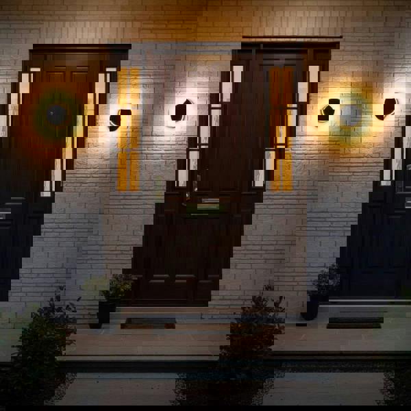black LED outdoor wall lamp mounted on a brick wall either side of a wooden front door 