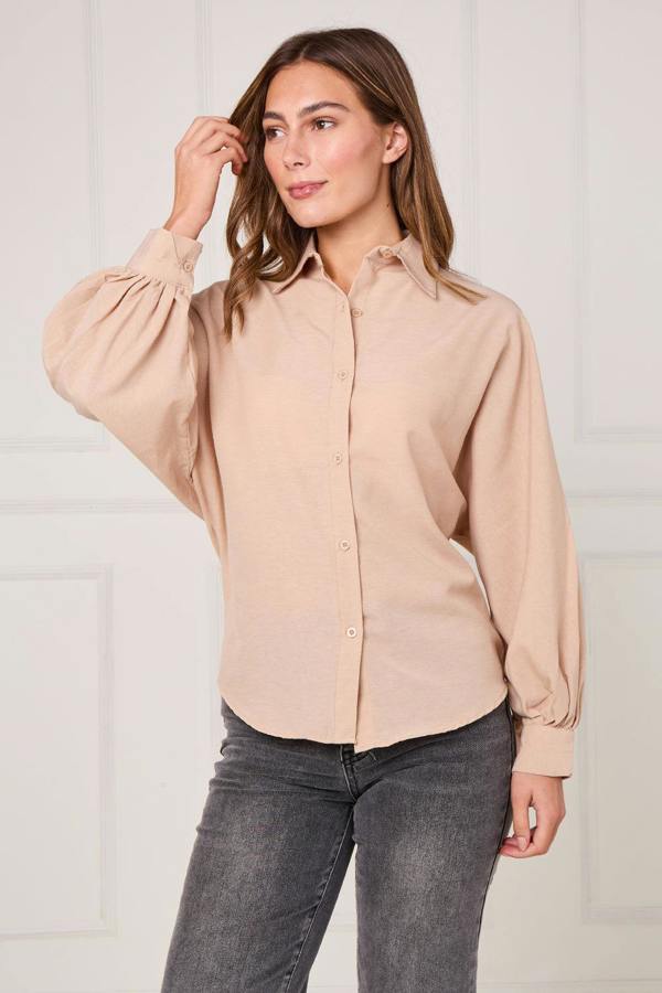 Woman wearing a beige blouse and gray pants against a plain background