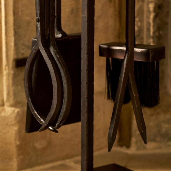Close-up of the wrought iron log grabber, fire poker prong, ash shovel, and bristle brush on the antiqued brown companion set.