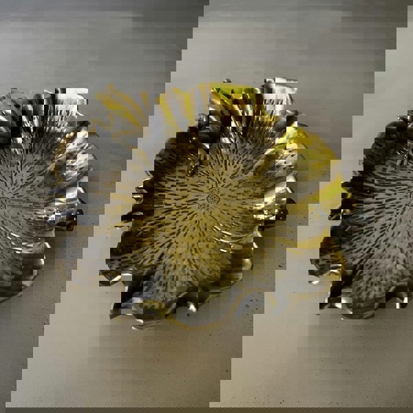 A white scented pillar candle with a twisted design, burning on a metal holder with a dark background.