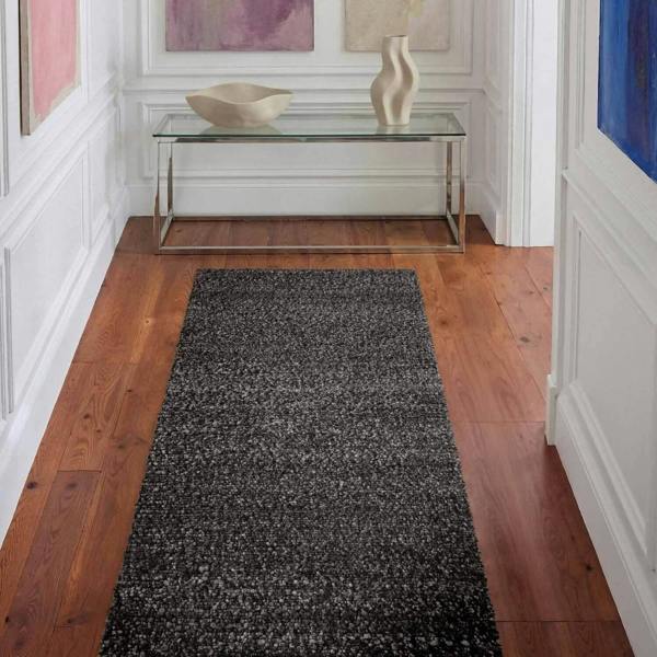 Black textured runner rug on a wooden floor with a glass console table and abstract art in the background.
