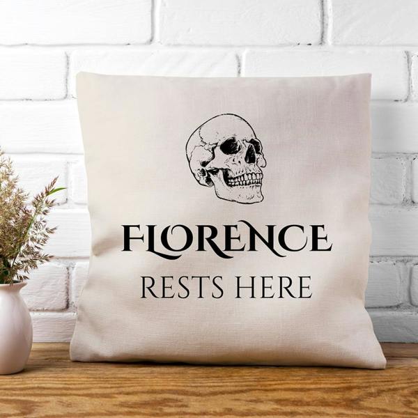 Square neutral cushion cover printed with a skull and Florence Rests Here text placed against a white painted brick wall