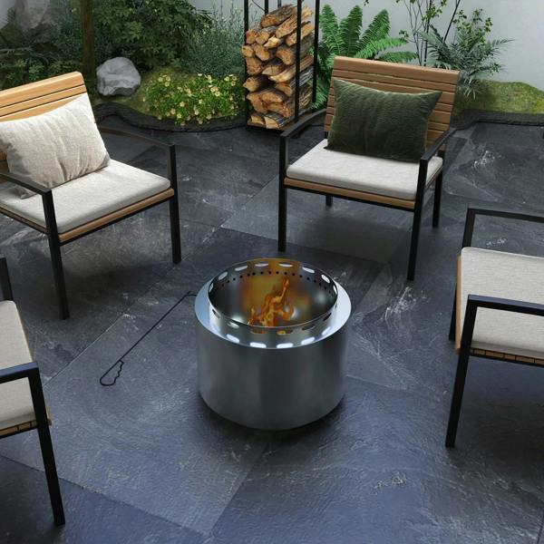 Stainless steel fire pit with flames in a garden patio near seating chairs