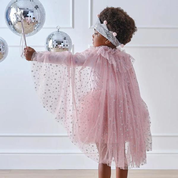 Back view of a child wearing a pink tulle fairy cape with silver stars while holding a silver wand next to disco balls.