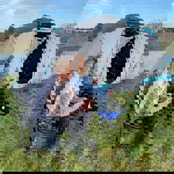 Image of OLPRO Camping Spike Stick Table being used by a couple outside a tent by a lake, with a glass of wine on top.