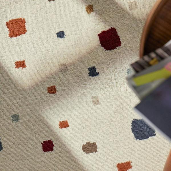 Close-up of a textured fabric with colorful square patterns and a wooden object in the corner.
