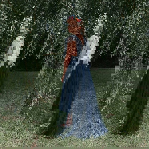 Girl in a white top and navy blue skirt standing in a grassy area with trees.