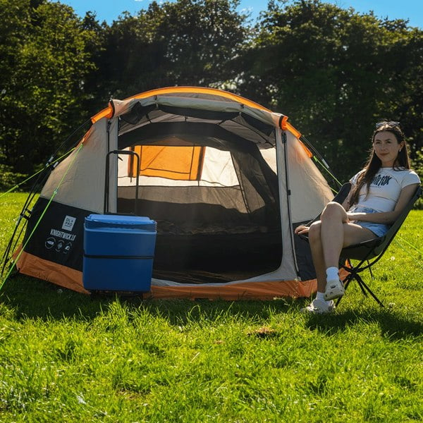 A young woman sits in front of an OLPRO Knightwick 3.0 3 Berth Tent at a festival