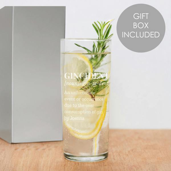 A tall, clear personalised highball glass by Abode Home & Gifts, filled with a gin drink, lemon slices, and a fresh rosemary sprig. The glass shows a frosted engraving of a "Gincident" dictionary definition ending with the name "Joanna", standing next to a grey gift box on a wooden board. A grey circular badge reads "Gift Box Included".