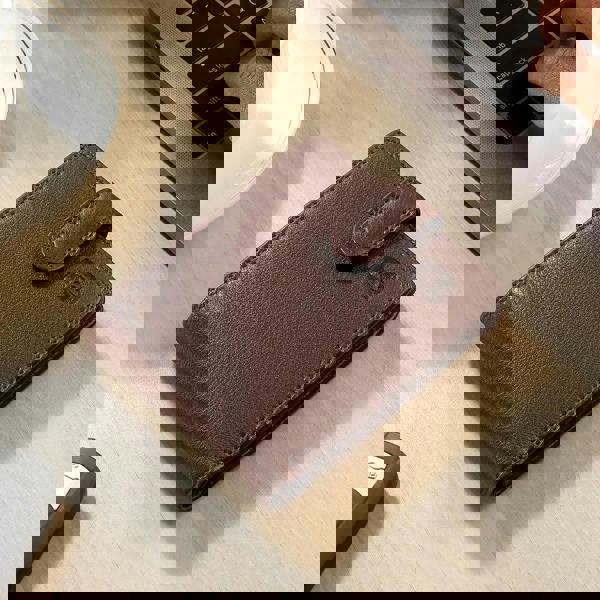 Brown leather wallet on a wooden desk with a laptop and glass of water in the background