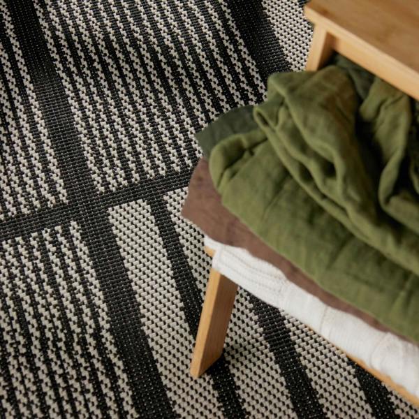 Green fabric on a wooden stool against a black and white geometric patterned rug