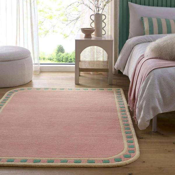 Pink rug with green border in a bedroom setting