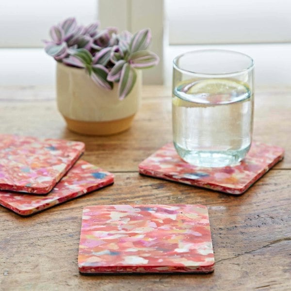 A multicoloured set of four recycled round plastic coasters on a table with a glass of water.