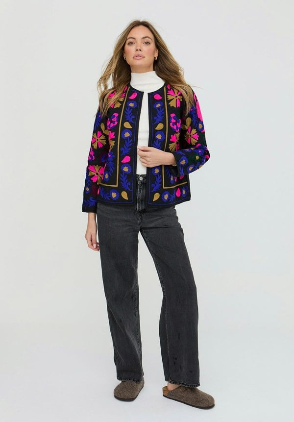 Woman wearing a colorful embroidered jacket on a white background