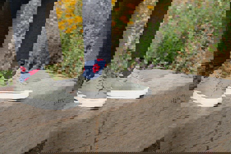 Person wearing green sneakers and dark pants with floral socks, standing on a wooden surface with a natural background.