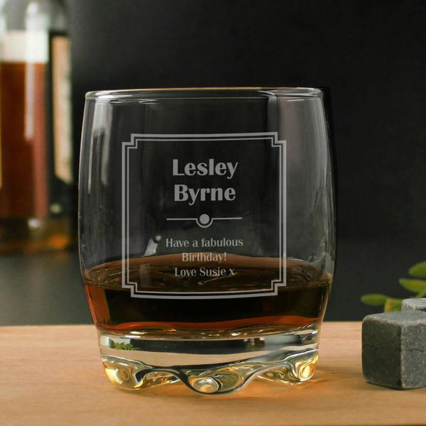 A personalised clear whisky glass featuring a geometric art deco border engraved with 'Lesley Byrne' and a birthday message, filled with amber spirit.