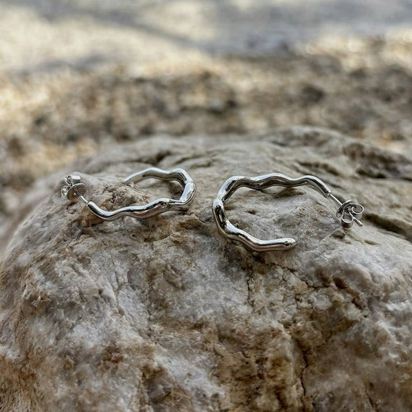 Silver open hoops, sculptural design. Displayed on a rock.