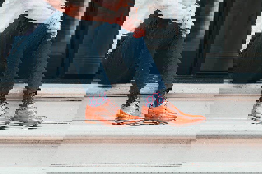 Person wearing brown shoes and funky patterned socks sitting on steps.