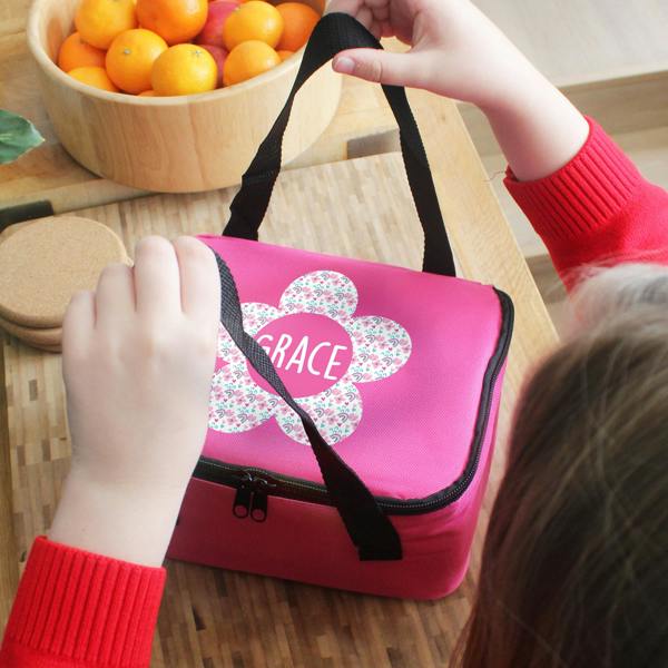 A child wearing a red sweater holds the black strap of a personalised pink flower lunch bag printed with the name Grace.