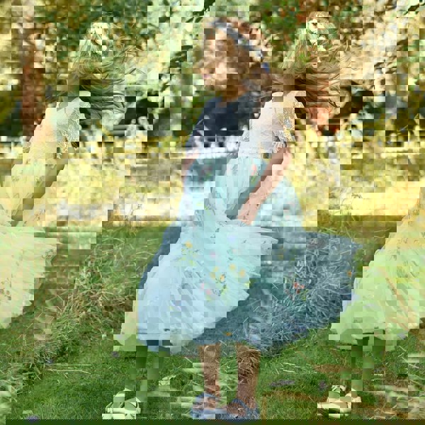 Young girl in a white lace top and light blue floral skirt standing in a grassy field.