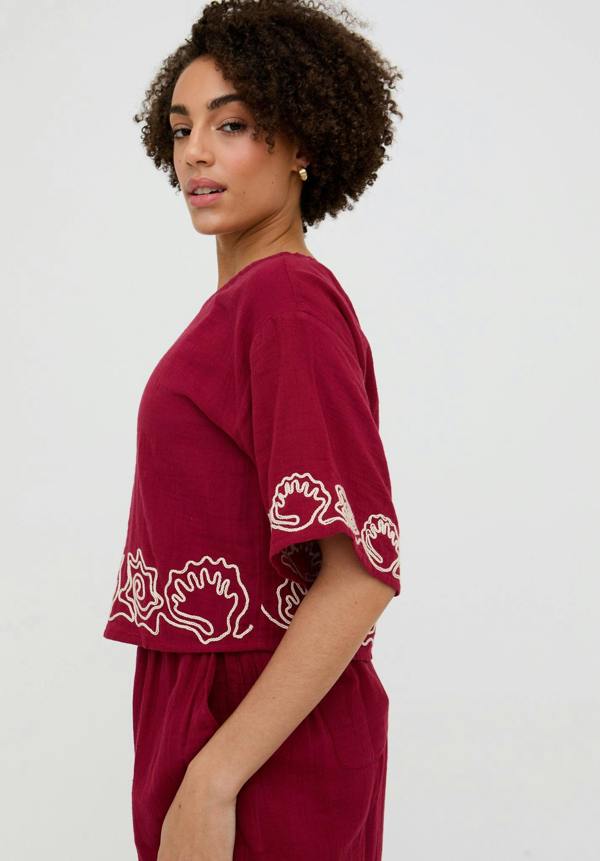 Woman wearing a burgundy top with white floral patterns on a plain background