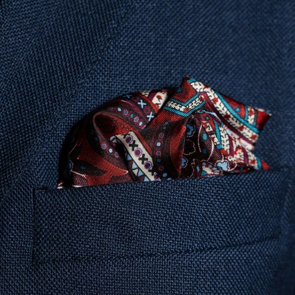 Intricate paisley design silk pocket square in burgundy, red, blue & cream by Otway & Orford folded in top pocket