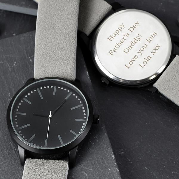 A personalised men's black watch by Abode Home & Gifts with a grey strap, showing the front face and the stainless steel back engraved with 'Happy Father's Day Daddy! Love you lots Lola xxx', styled on a slate surface.