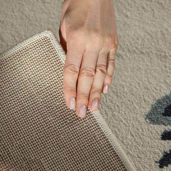 Hand holding a textured beige rug corner on a neutral background