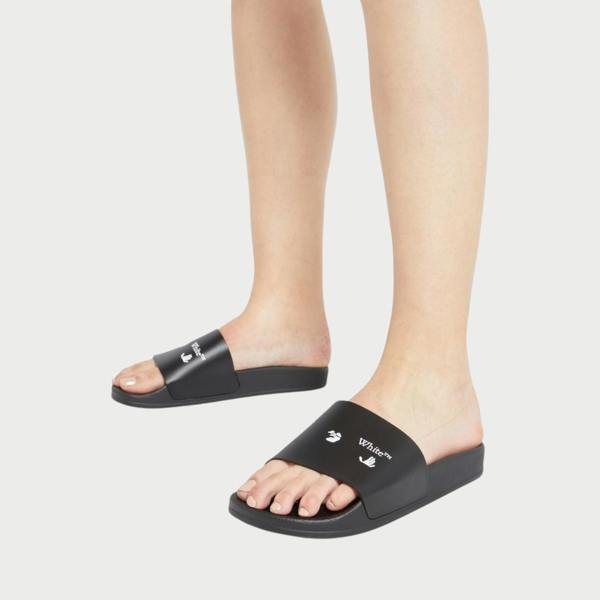 Supplied Fashion black slides with white Swimming Man logo worn on feet against a plain light grey background