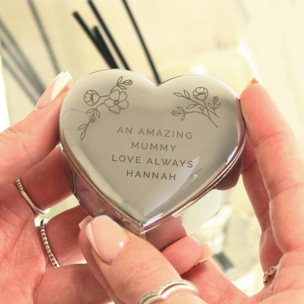 A close-up view of a high-shine nickel-plated heart trinket box from Abode Home & Gifts, engraved with a delicate floral motif and a custom message.