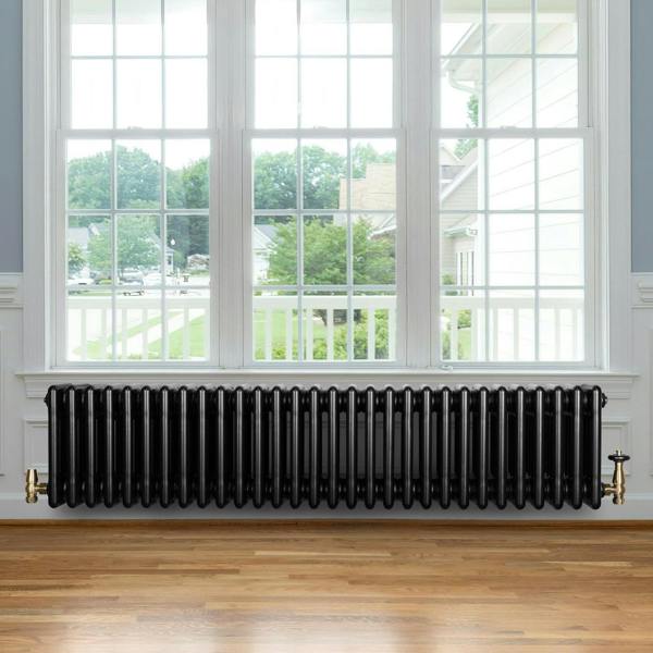 Traditional black 4 column radiator with brass valves, showcasing a sleek design against a bright window backdrop and wooden floor