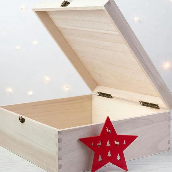 Open natural wooden Christmas Eve box with hinged lid showing empty interior alongside red star ornament and candy cane