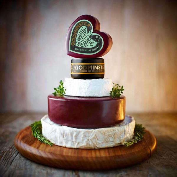 A five-tier organic British celebration cheese cake tower topped with a heart-shaped cheddar on a wooden board.