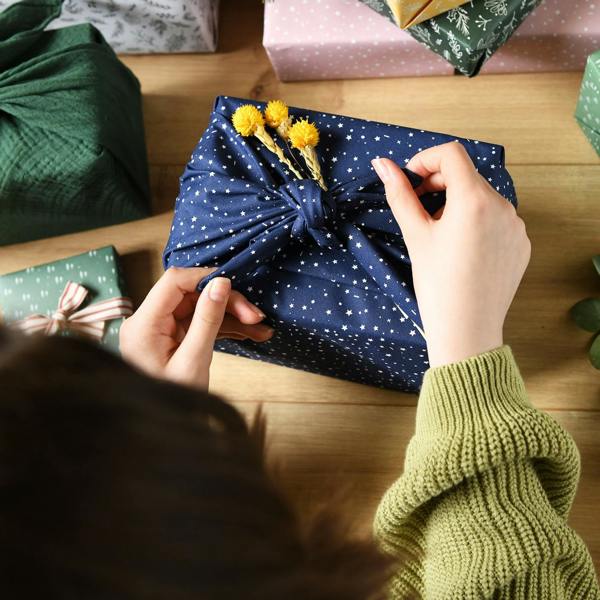 Person tying a reusable navy fabric gift wrap printed with white stars around a present