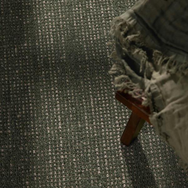Textured green carpet with a wooden stool and a blanket on it