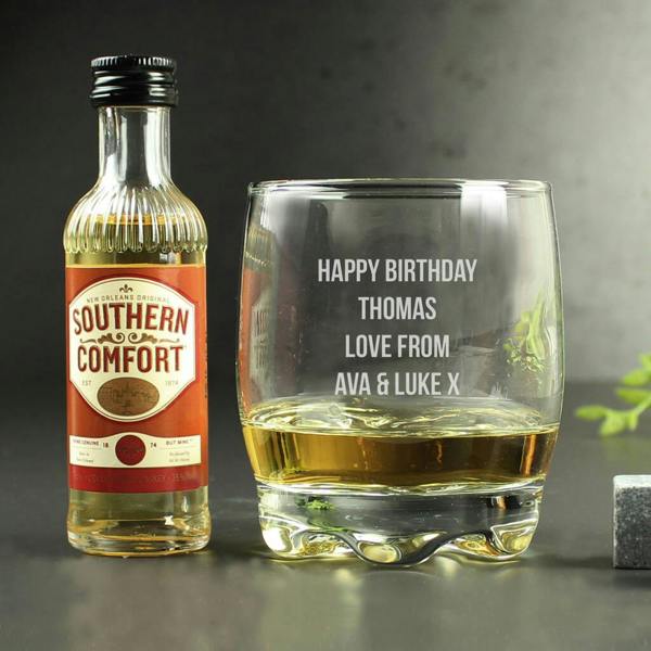 A personalised whiskey tumbler engraved with 'HAPPY 30th BIRTHDAY MATT CHEERS!' next to a miniature bottle of Southern Comfort and an open silver gift box on a dark surface.