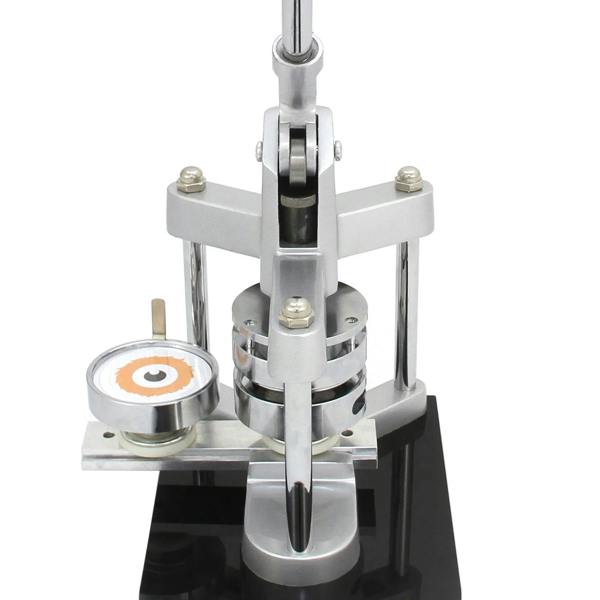 Silver metal badge making machine with a circular press, featuring a clear base and a colorful badge design ready for pressing