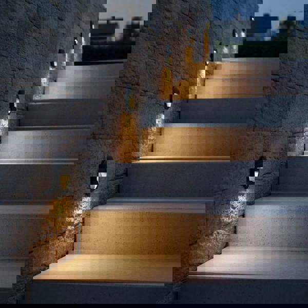 black outdoor stair light mounted on a stone wall alongside outdor steps 
