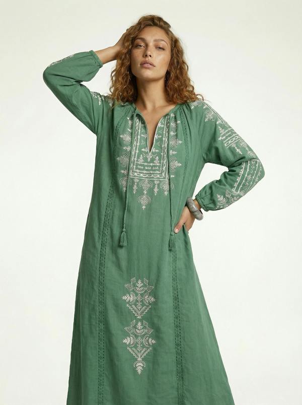 Woman wearing a green embroidered dress on a white background