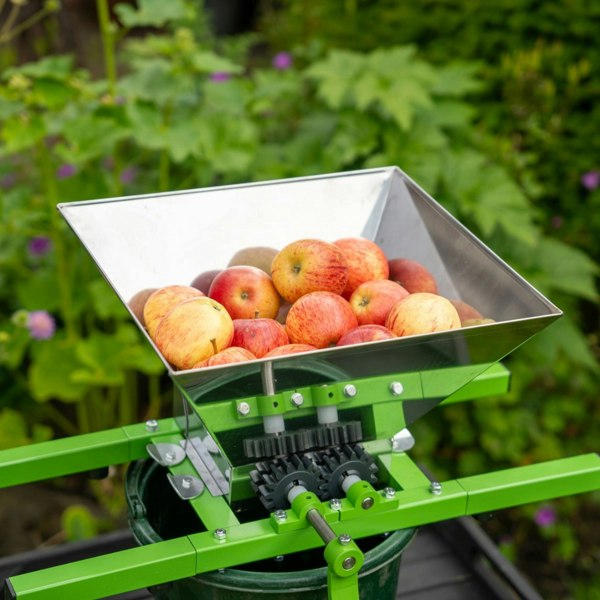 Stainless steel fruit crusher with a large hopper filled with red apples, mounted on a green frame for easy pressing