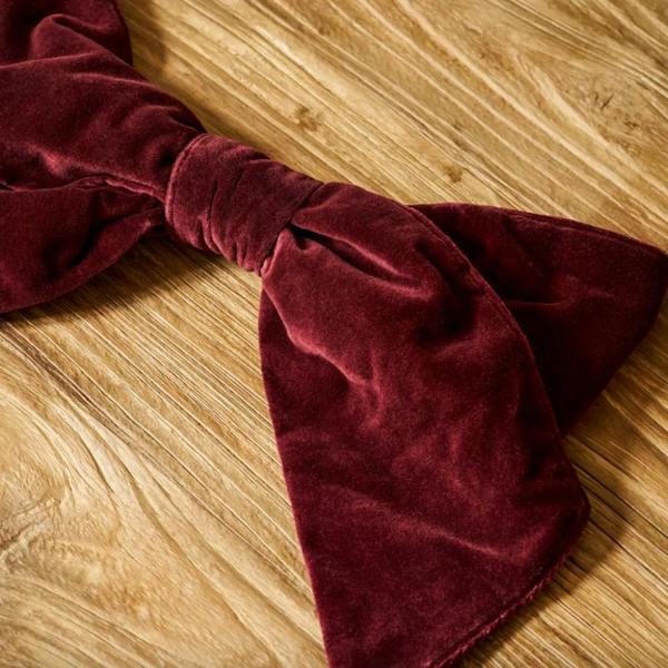 Close-up of a rich berry red cotton velvet Christmas bow resting on a natural wooden surface.