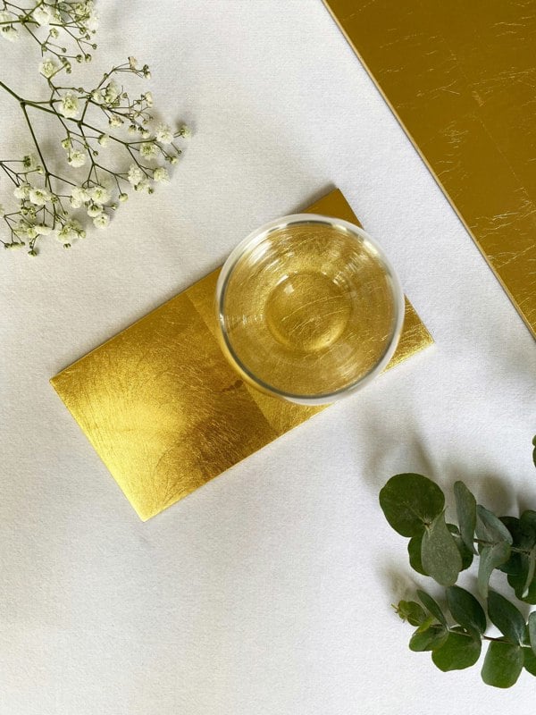 Gold Leaf Double Coaster on a white table surface with a glass on it