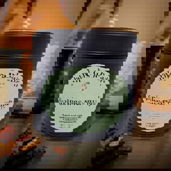 Candle tin labeled 'Ralph's Orchard frankincense & myrrh' on a wooden surface.