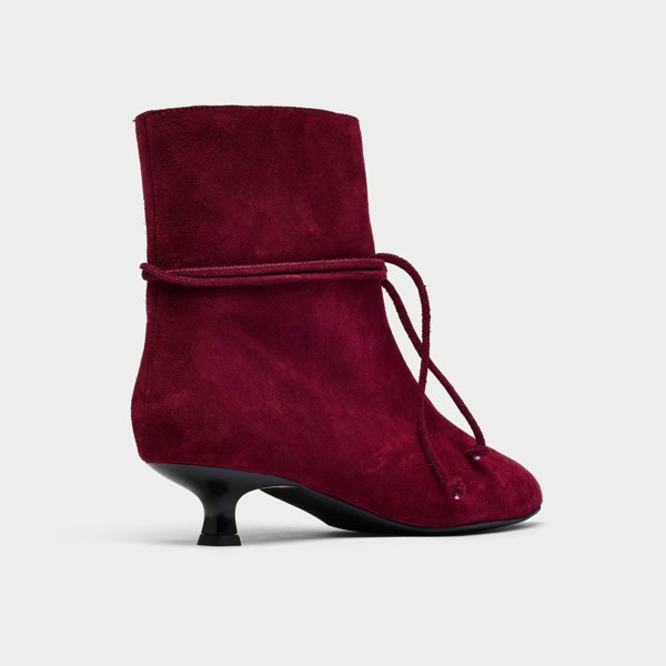 Maroon suede ankle boot with a black heel on a light gray background