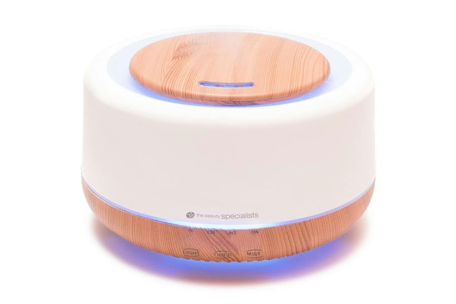 The Rio ALORA Aroma Diffuser, Humidifier & Night-Light features a round white body with light wood accents, control buttons, and a glowing blue base for ambiance.